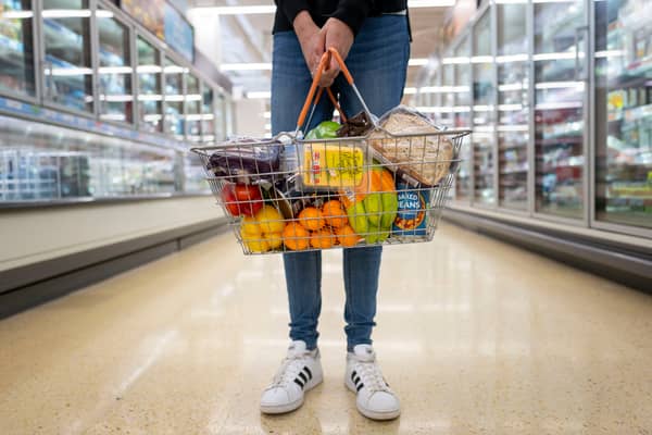 A woman holds a basket of goods in a supermarket.