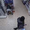 Video grab of Nicolae Boia crouched behind a trolley and filling his bag with unpaid for goods.