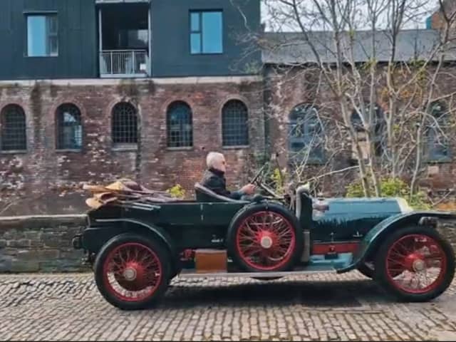 An antique car driving down a cobbled street
