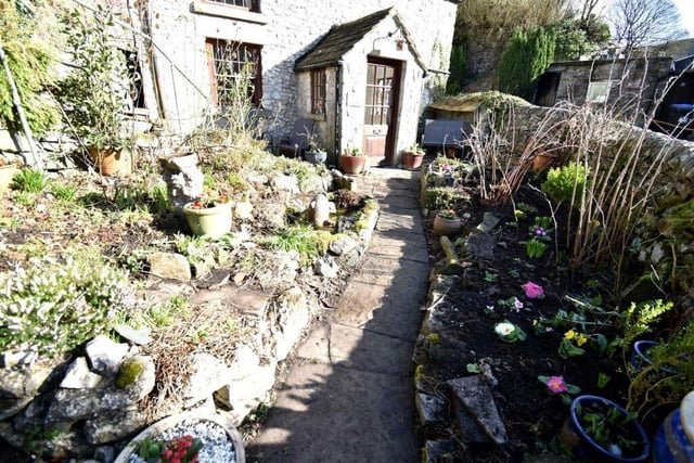 There is a formal cottage garden  with flowers and shrubs and a stone paved pathway to the front door of the house.