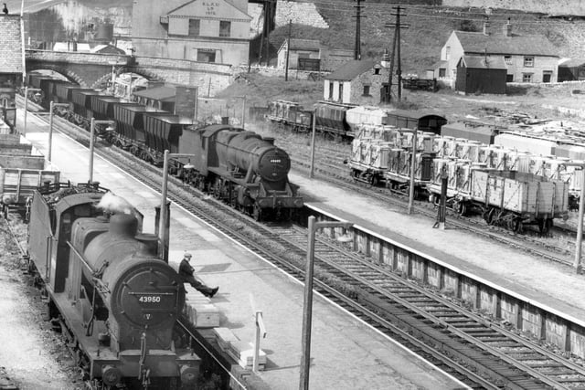Peak Forest station looking north is 36 miles from Derby on the Midland Railway's Manchester line. A train of limestone empties is on the main line with Stanier 8F No.48605 in charge. The local goods train is being worked by 4F Class 0-6-0 No.43950 whose driver has taken the oportunity to take a brief siesta. The tip in the background consists of waste from the limestone workings, August 1960. (Photo by Rail Photo/Construction Photography/Avalon/Getty Images)