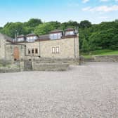 The detached stone-built home with woodland as a backdrop.