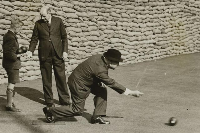 Members of the Chesterfield Bowlng Club, undetered by the nearby grimly piled sandbags of an air raid sheter, concentrating on their game.