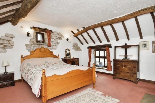 A paneled door with a thumbnail latch opens into bedroom one. The bedroom has an open gritstone fireplace and exposed beams to the vaulted ceiling.