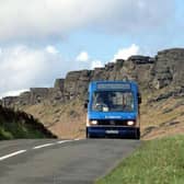 A bus travels along a road below Stanage Edge, near Hathersage in Hope Valley