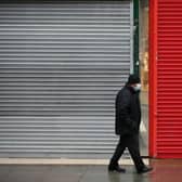 A man wearing a face mask walks past the shutters of temporarily-closed stores. Picture by David Cliff/NurPhoto via Getty Images.