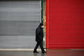 A man wearing a face mask walks past the shutters of temporarily-closed stores. Picture by David Cliff/NurPhoto via Getty Images.