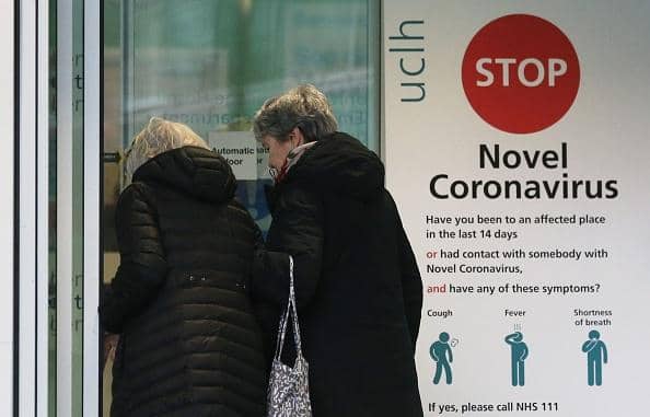 Two women walk past a sign providing guidance information about novel coronavirus (COVID-19) at one of the entrances to University College Hospital in London. (Photo by ISABEL INFANTES/AFP via Getty Images)