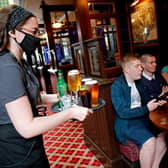 A member of bar staff wearing PPE (personal protective equipment) in the form of a face mask, serves seated customers drinks inside the Wetherspoon pub. (Photo by Tolga AKMEN / AFP) (Photo by TOLGA AKMEN/AFP via Getty Images)