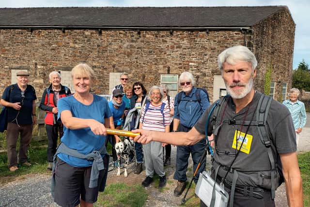 Buxton u3a walk leader Charles Huff handing over the relay baton to Jan Smith of New Mills u3a at New Mills Marina, watched by members of Buxton u3a