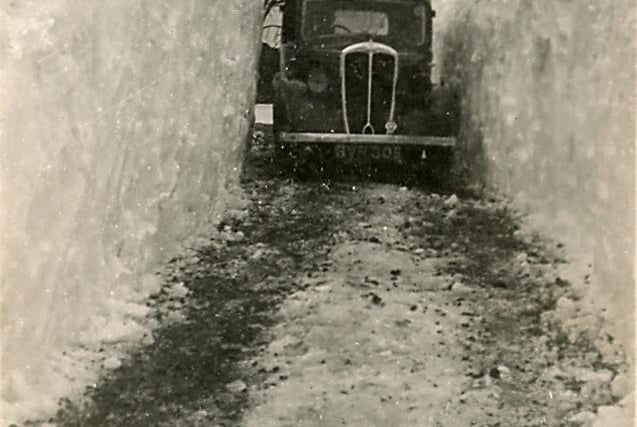In 1940, a vehicle navigates a road cut through very deep snow drifts at Combs