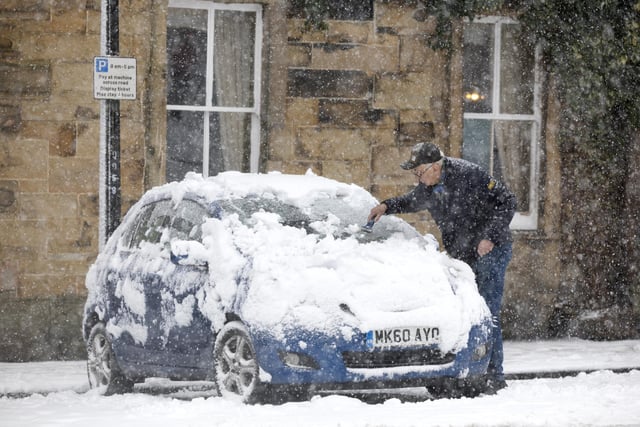 A man clears snow off a car. Photo RKP Photography