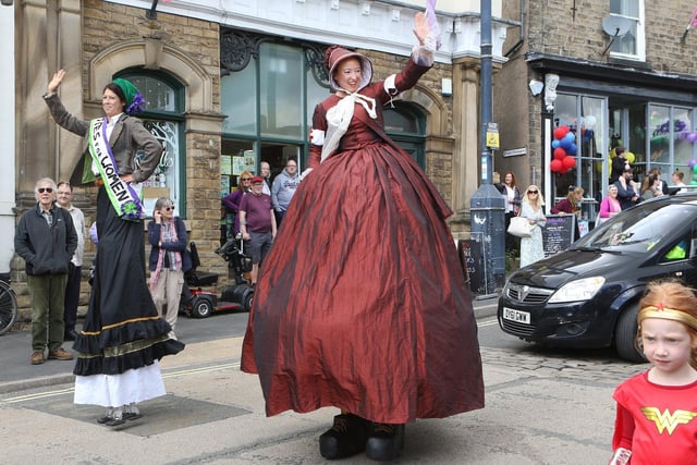 Suffragette stilt walkers waving during New Mills carnival