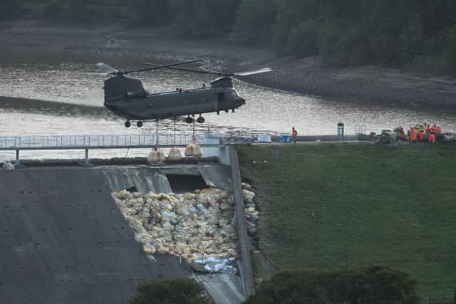 An RAF Chinook helicopter drops more bags of aggregate on the damaged section of spillway of the Toddbrook Reservoir dam above the town of Whaley Bridge in northern England on August 4, 2019 (photo by OLI SCARFF / AFP).