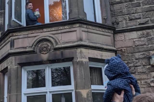 Nick in the first-floor window of his home with Olivia while his brother Anthony holds up six-month-old son Ted