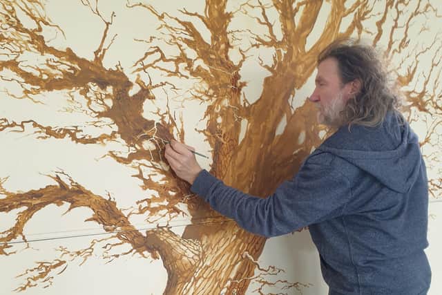 Local artist Chris Hollis working will be adding to his tree painting as donations come in.