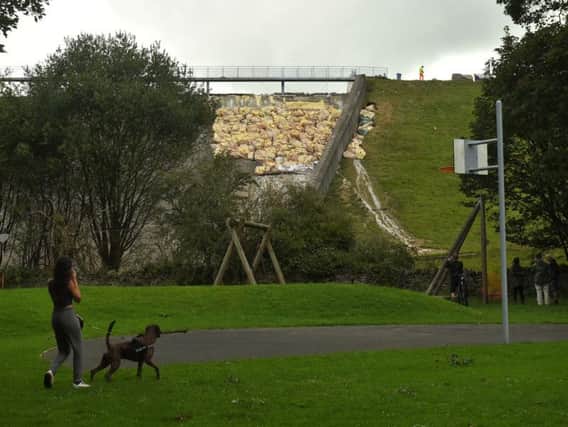A woman walks her dog below the damaged section of the Toddbrook Reservoir dam, which is filled with bags of aggregate to reinforce the structure. Photo: OLI SCARFF/AFP/Getty Images.
